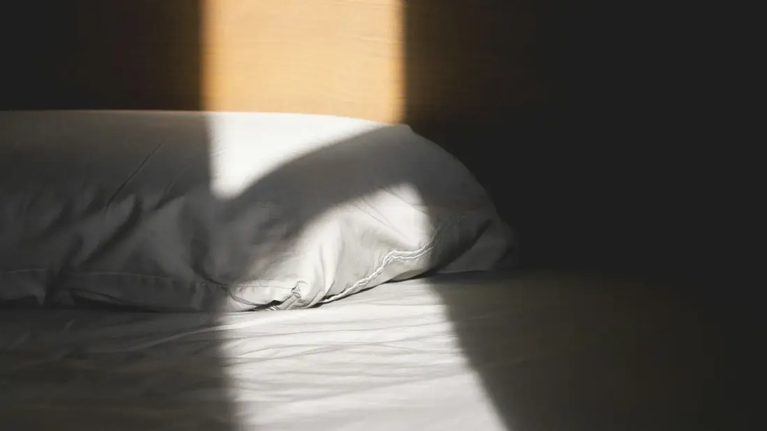 White pillow against a wooden headboard in morning light
